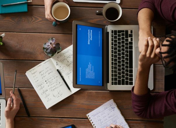Group of coworkers discussing business strategies with laptops and tablets in a modern office setting.