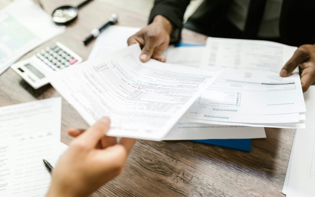 Two professionals exchanging documents in an office setting, focusing on paperwork and data analysis.